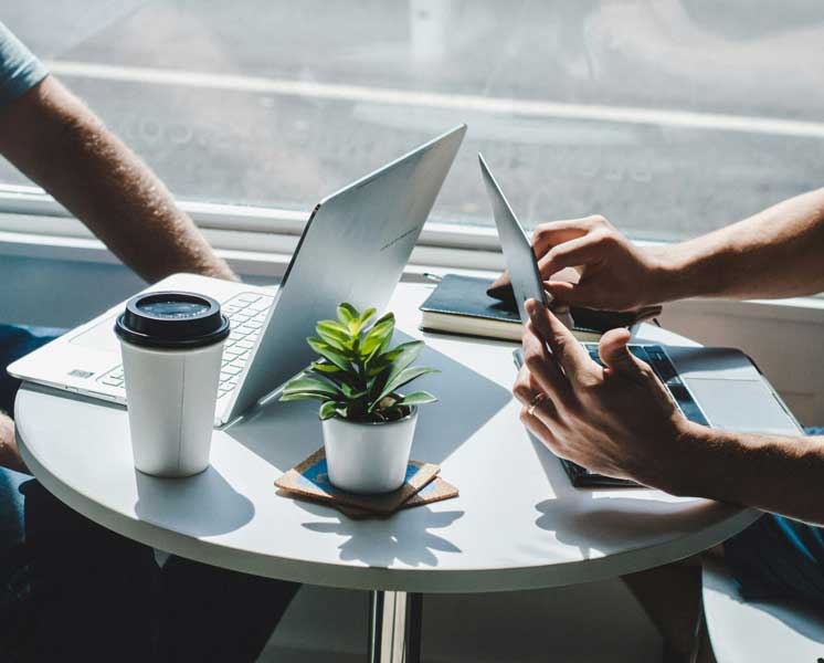 Duas pessoas conversando em uma mesa de cafeteria com seus notebooks abertos.
