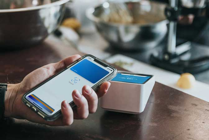 Cliente pagando a conta na cafeteria com seu cartão se aproximando da máquina.