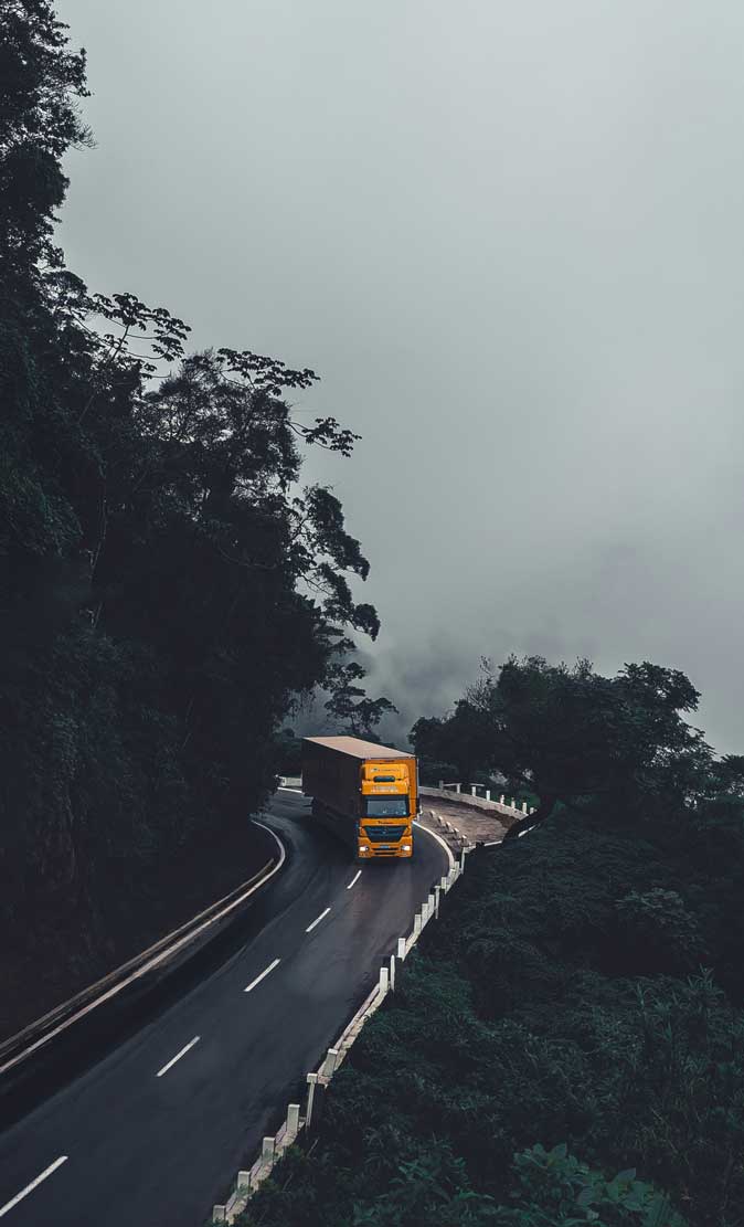 Caminhão amarelo trafegando na serra com neblina.